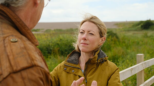 Charlotte listening to a local resident with a green natural background