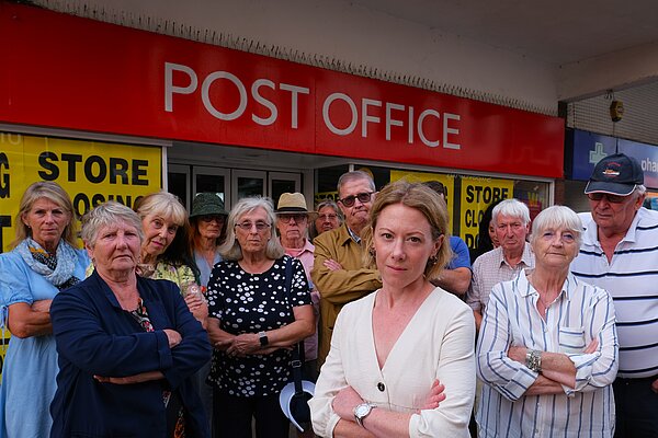 Charlotte FitzGerald and a group of campaigners stand in front of a large red Post Office sign.