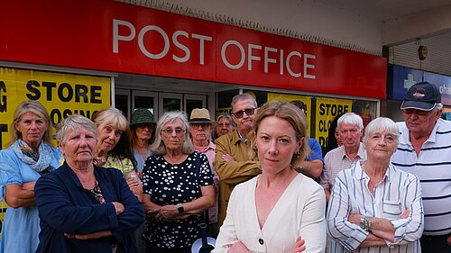 Charlotte FitzGerald and a group of campaigners stand in front of a large red Post Office sign.