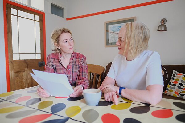 Charlotte talking to a local resident at a kitchen table holding bill paperwork