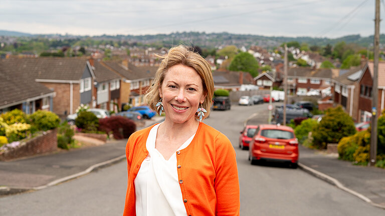 Charlotte FitzGerald smiling at the camera standing in a residential street with green hills in the distance