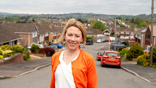 Charlotte FitzGerald in an orange cardigan and white shirt smiling while standing in a residential street